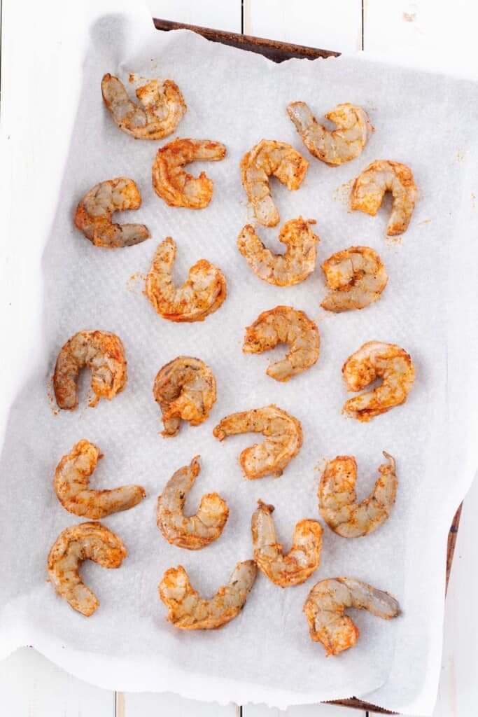 Raw shrimp spiced and spread on a parchment lined baking sheet.