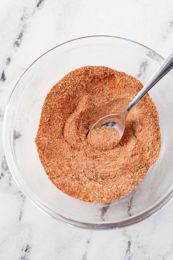 Mixing the spices together with a spoon in a glass mixing bowl.