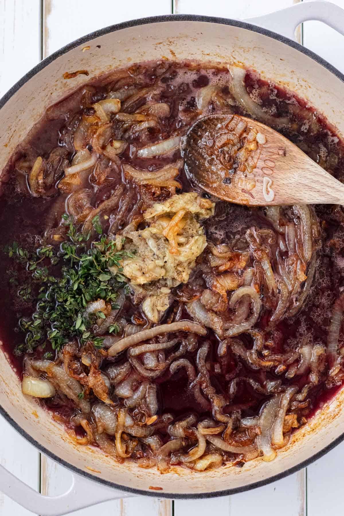 Adding the roasted garlic, thyme, and red wine to deglaze the pan.