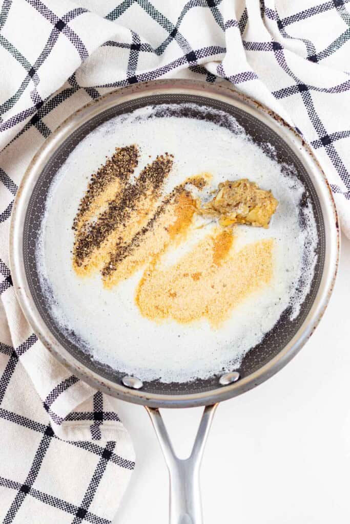 Adding the spices and roasted garlic to the melted butter in a pan.