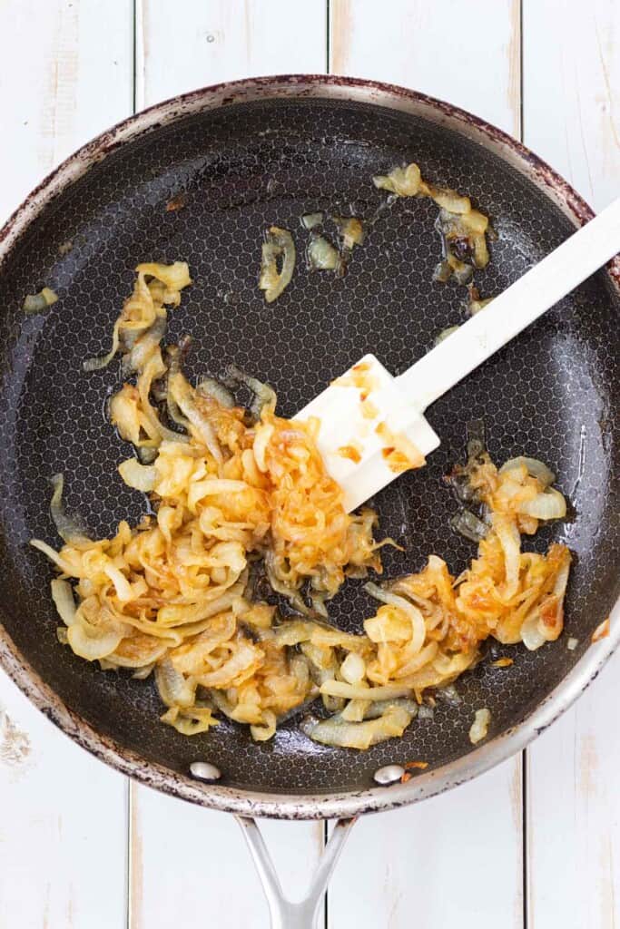 A frying pan with fully caramelized onions and a spatula.