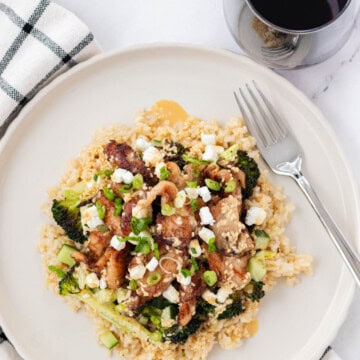 Chicken and rice bowl on a plate with a fork and a glass of wine.