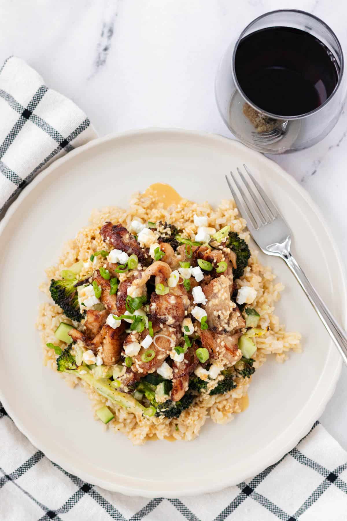 Chicken and rice bowl on a plate with a fork and a glass of wine.