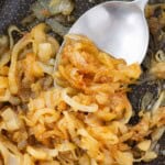 A silver spoon scooping golden brown caramelized onions from a pan.