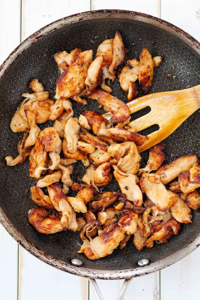 Frying the chicken in a frying pan with a wooden spatula.