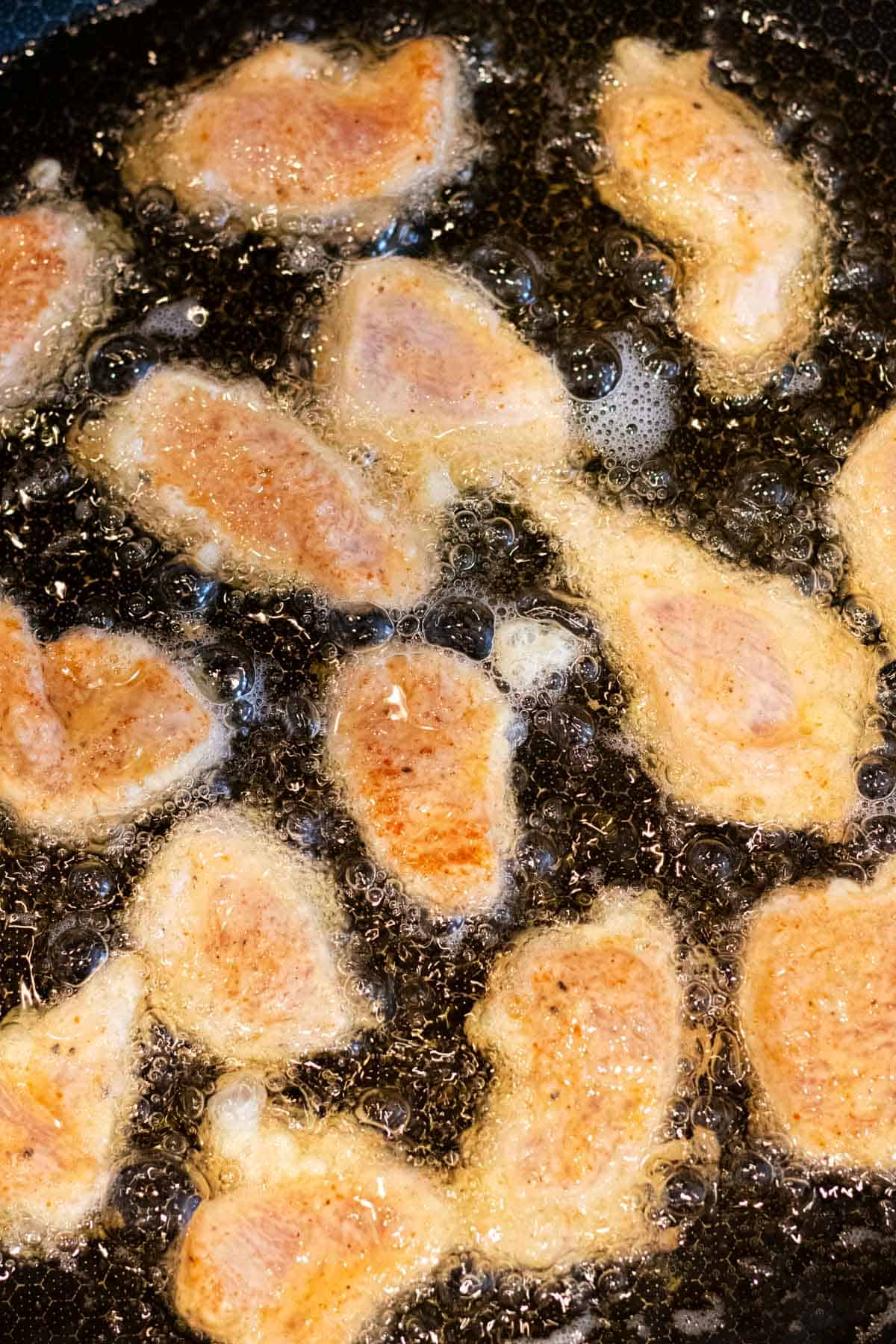 Frying the lightly breaded chicken pieces in vegetable oil.