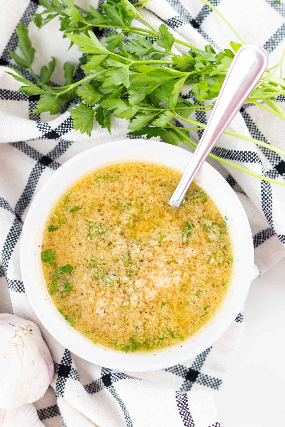 A white bowl filled with garlic parmesan sauce with parsley and garlic on the side.