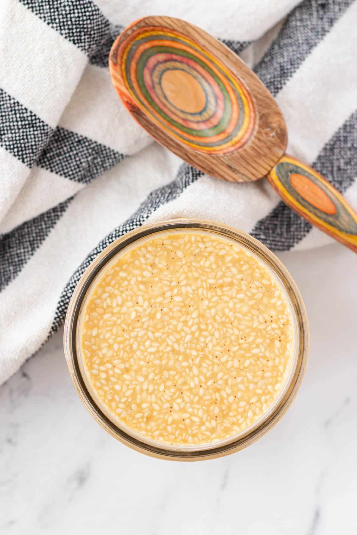 A jar full of roasted sesame sauce and a serving spoon on the side.