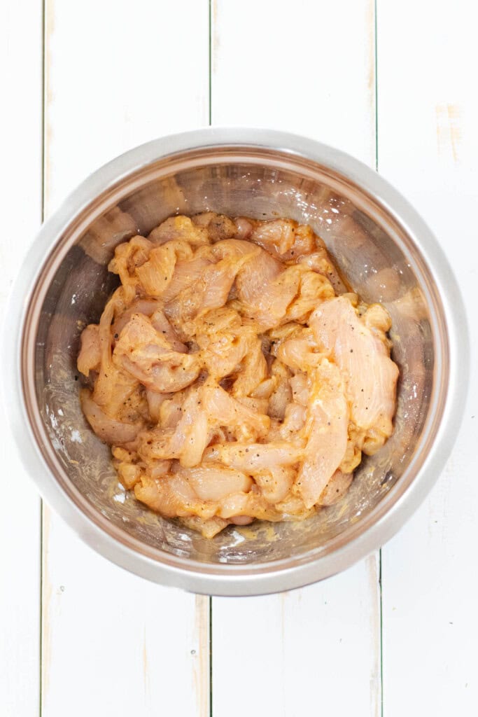 Marinating the chicken breast strips in a stainless steel bowl.