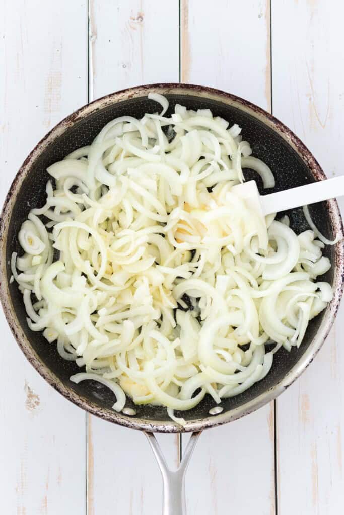 Adding onions to a frying pan.