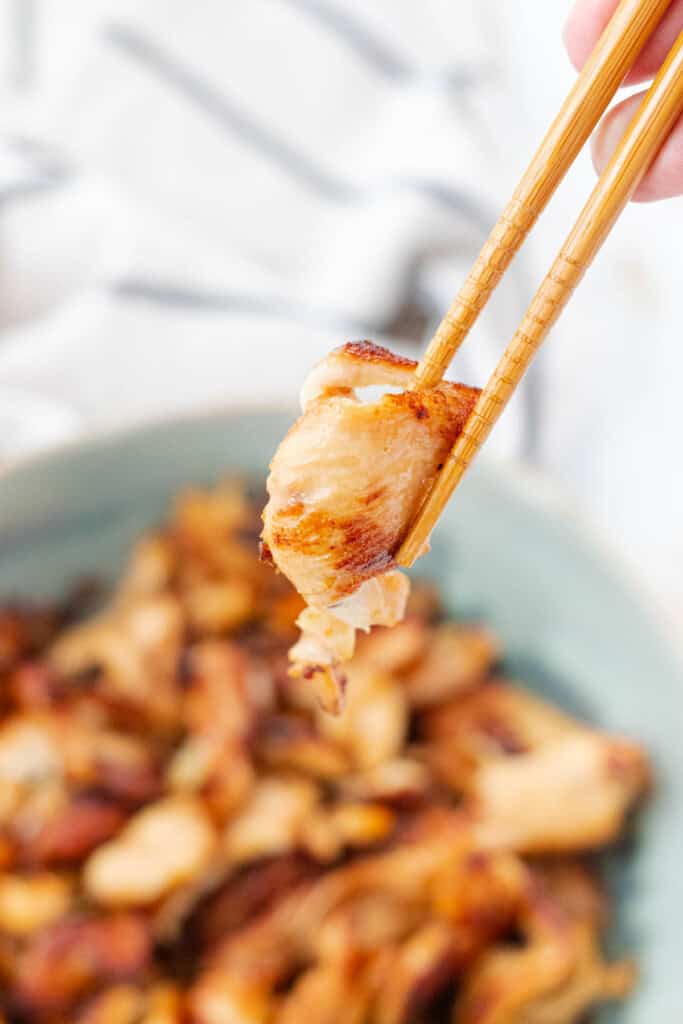 Holding a piece of the chicken with a pair of chopsticks.