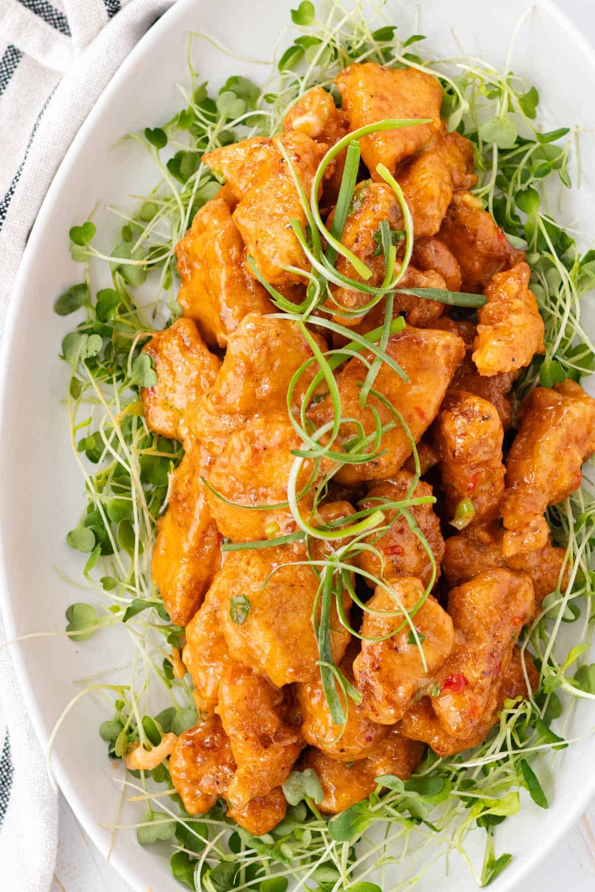Plating the bang bang chicken by laying it on a plate on top of a bed of arugula sprouts.