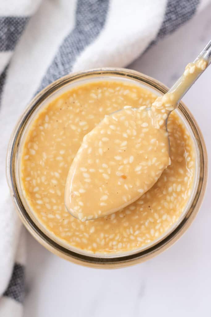 A spoon holding a spoonful of sauce over a jar.