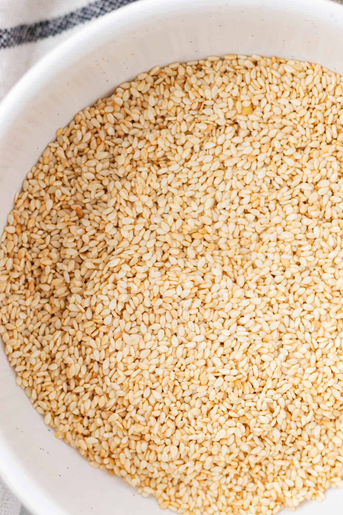 A white bowl filled with freshly roasted sesame seeds.