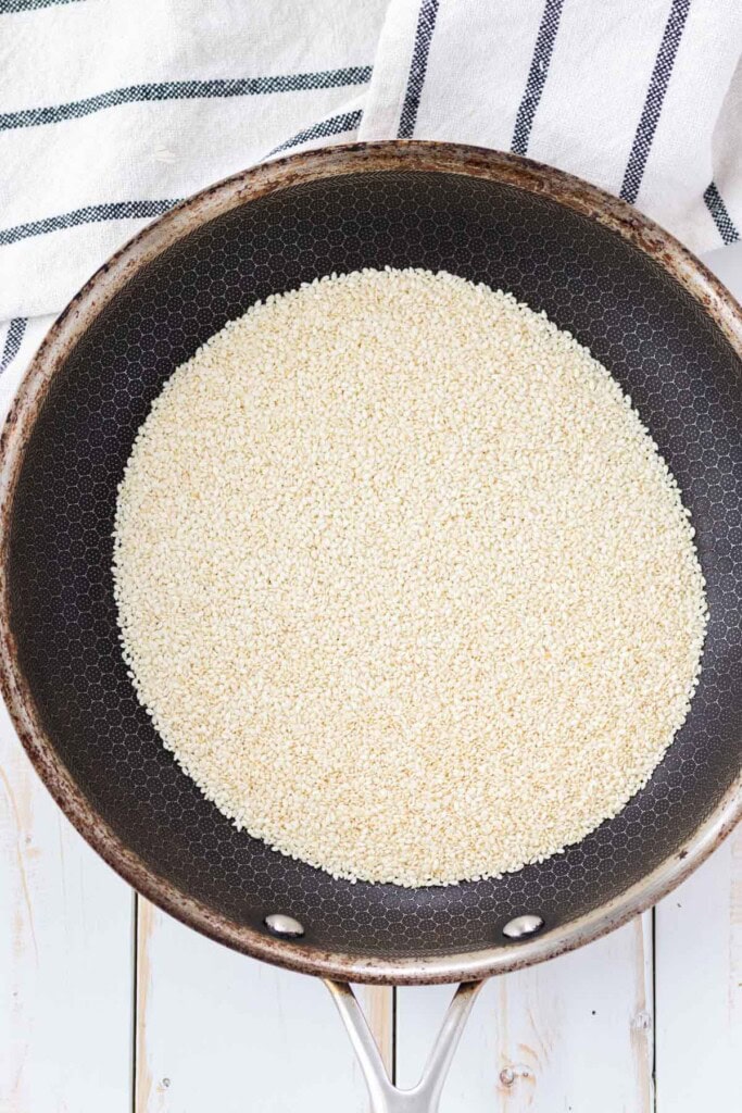 Adding raw sesame seeds to a frying pan.