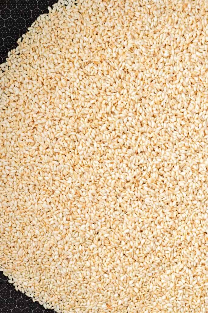 Golden brown toasted sesame seeds in a frying pan.