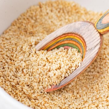A colorful wooden spoon taking a scoop of toasted sesame seeds.