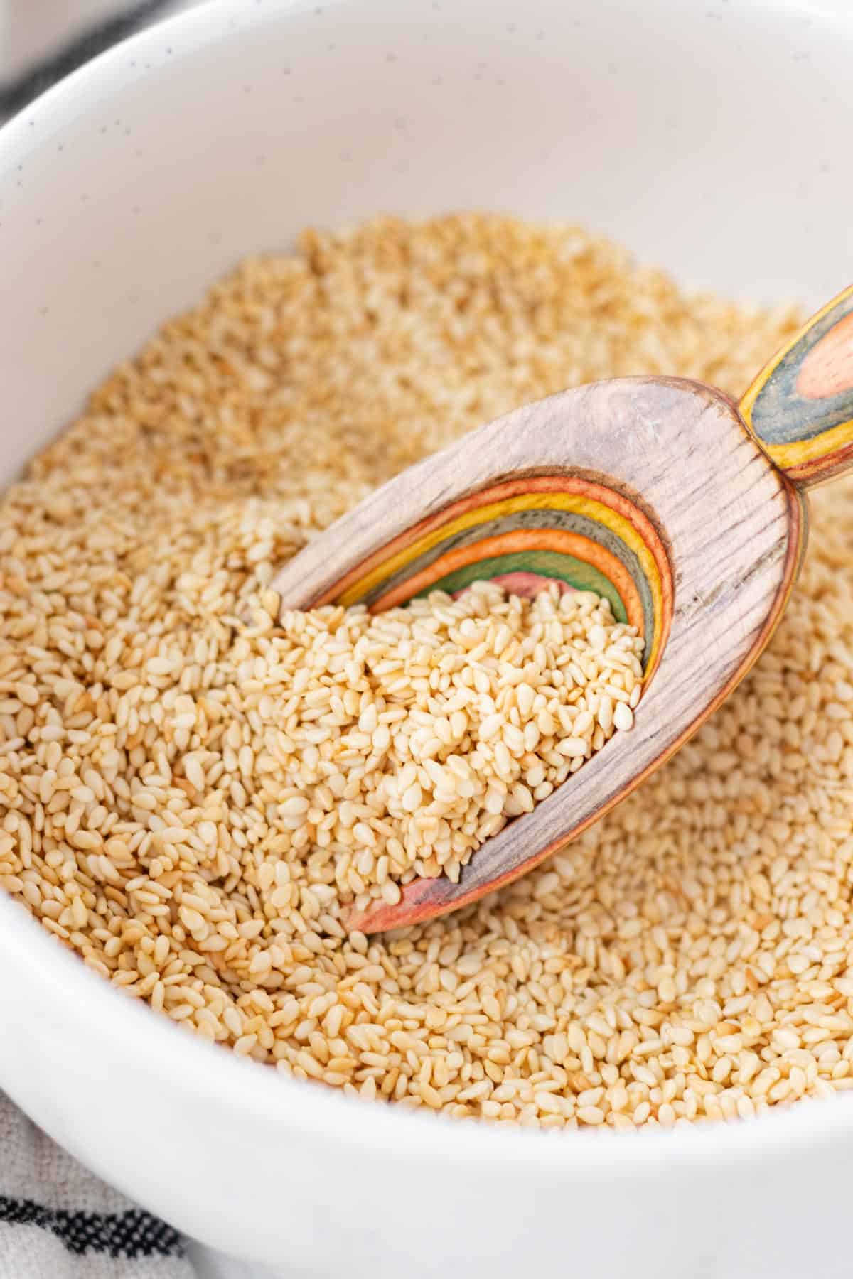 A colorful wooden spoon taking a scoop of toasted sesame seeds.