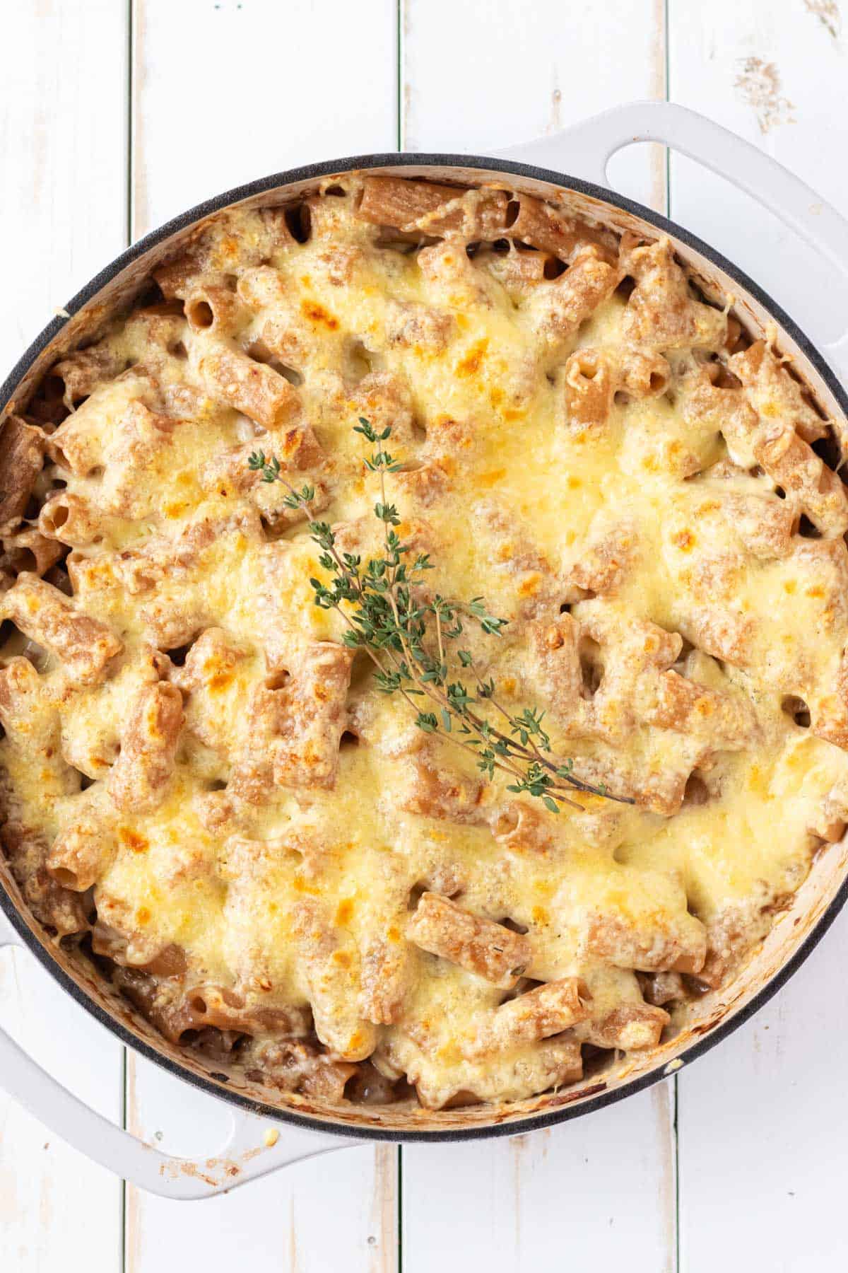 A white sauté pan filled with french onion pasta with swiss cheese melted on top.