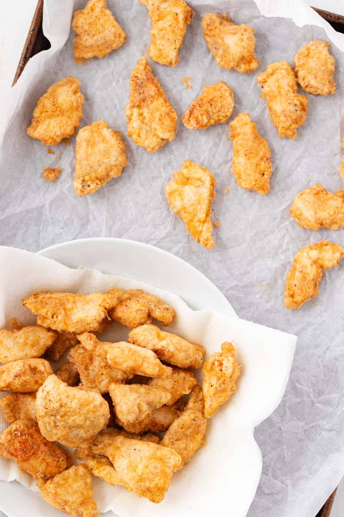 Transferring the fried chicken pieces from a paper towel lined bowl to a baking sheet lined with parchment.