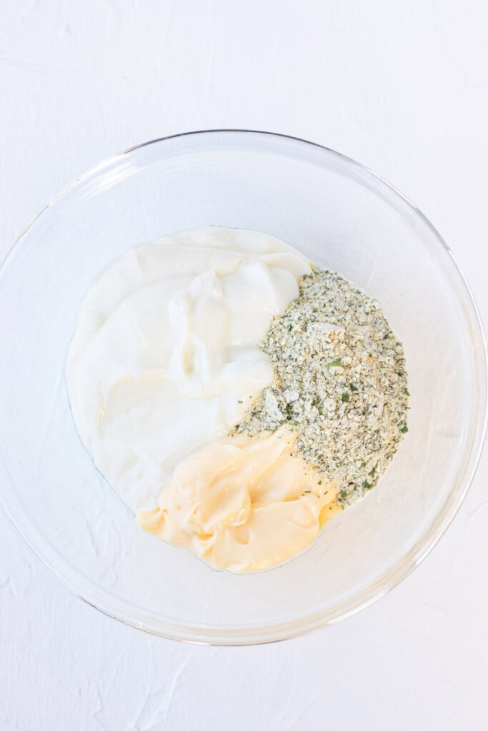 Adding the mayo, greek yogurt, and ranch powder to a bowl.