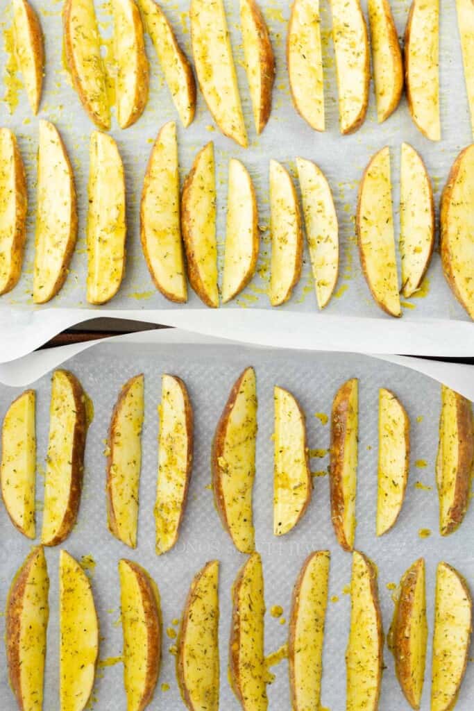 Marinated wedges arranged on sheet pans lined with parchment paper.