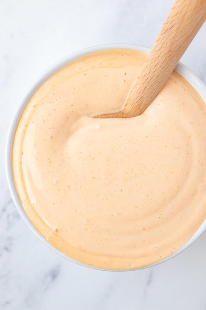 A white bowl filled with spicy mayo and a wooden spoon.