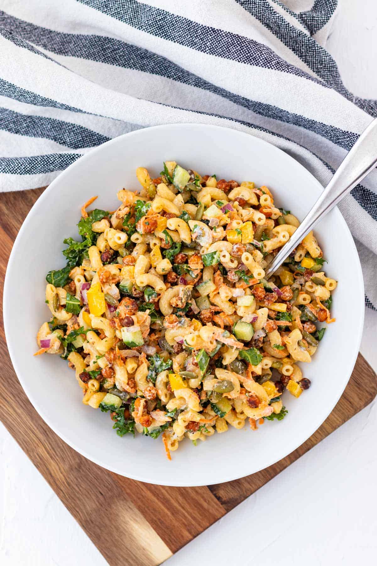 A white bowl full of buffalo chickpea pasta salad on a wooden board.