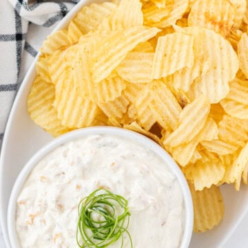 French onion chip dip in a white bowl with ruffle chips on the side.
