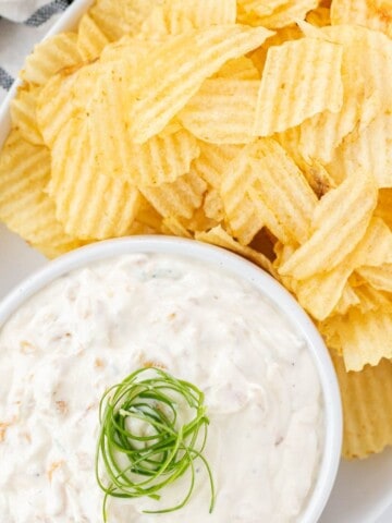 French onion chip dip in a white bowl with ruffle chips on the side.