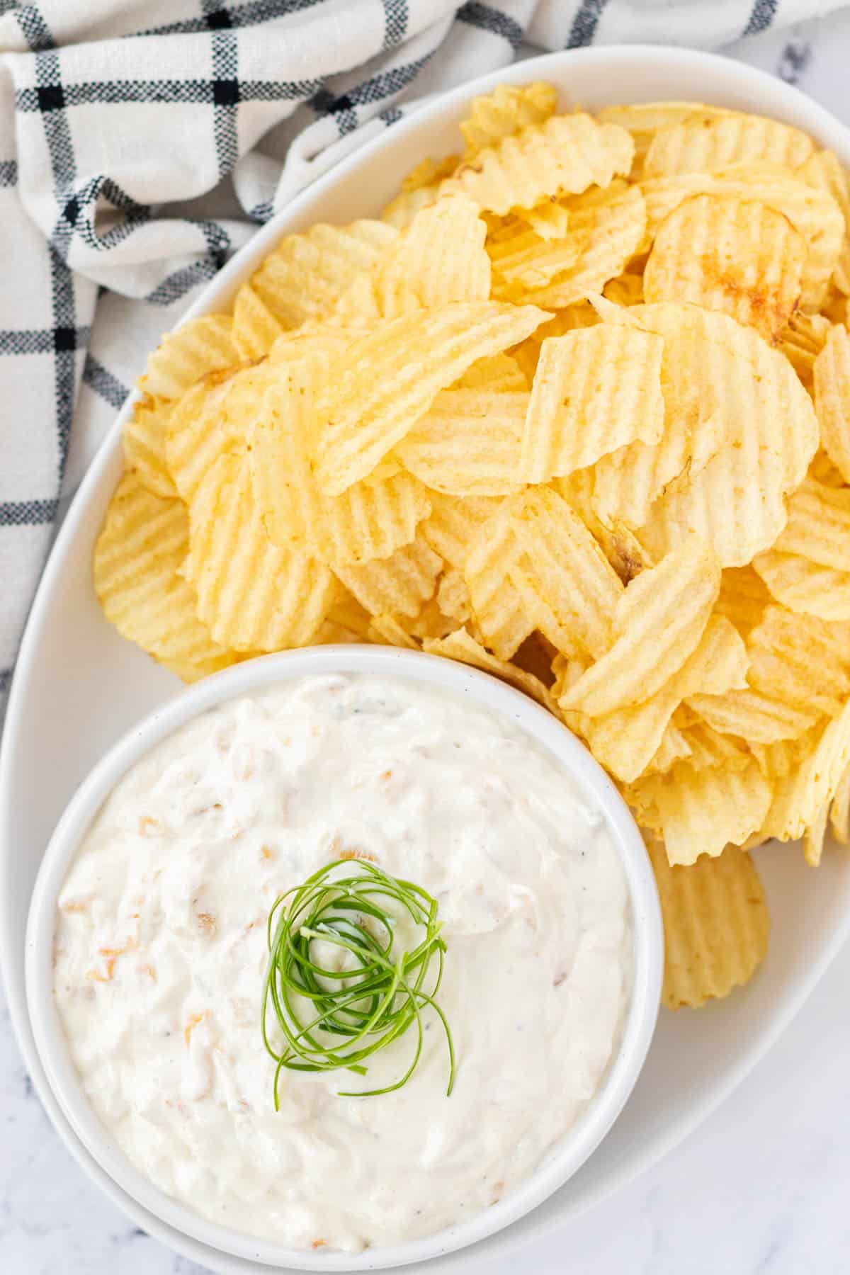 French onion chip dip in a white bowl with ruffle chips on the side.
