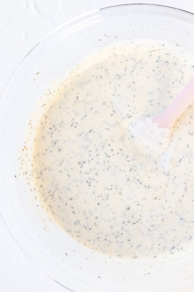Stirring the ranch dressing together with a spatula in a glass bowl.