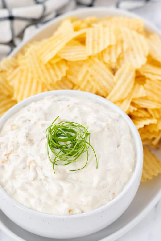 A white bowl full of onion dip with curled green onions on top.