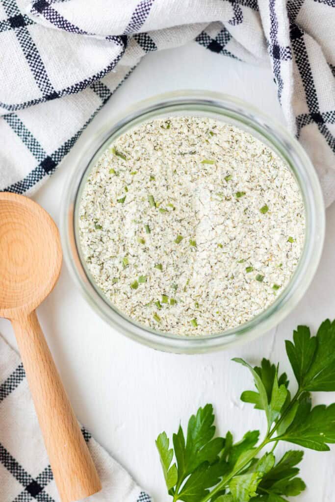 A jar of homemade ranch seasoning with a wooden serving spoon on the side.