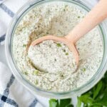 A round wooden serving spoon in a jar of ranch seasoning mix.