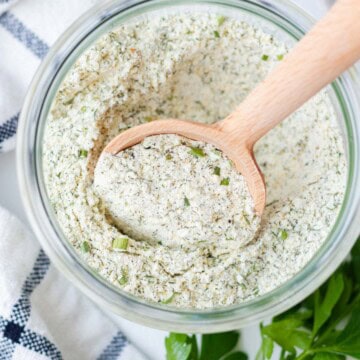 A round wooden serving spoon in a jar of ranch seasoning mix.