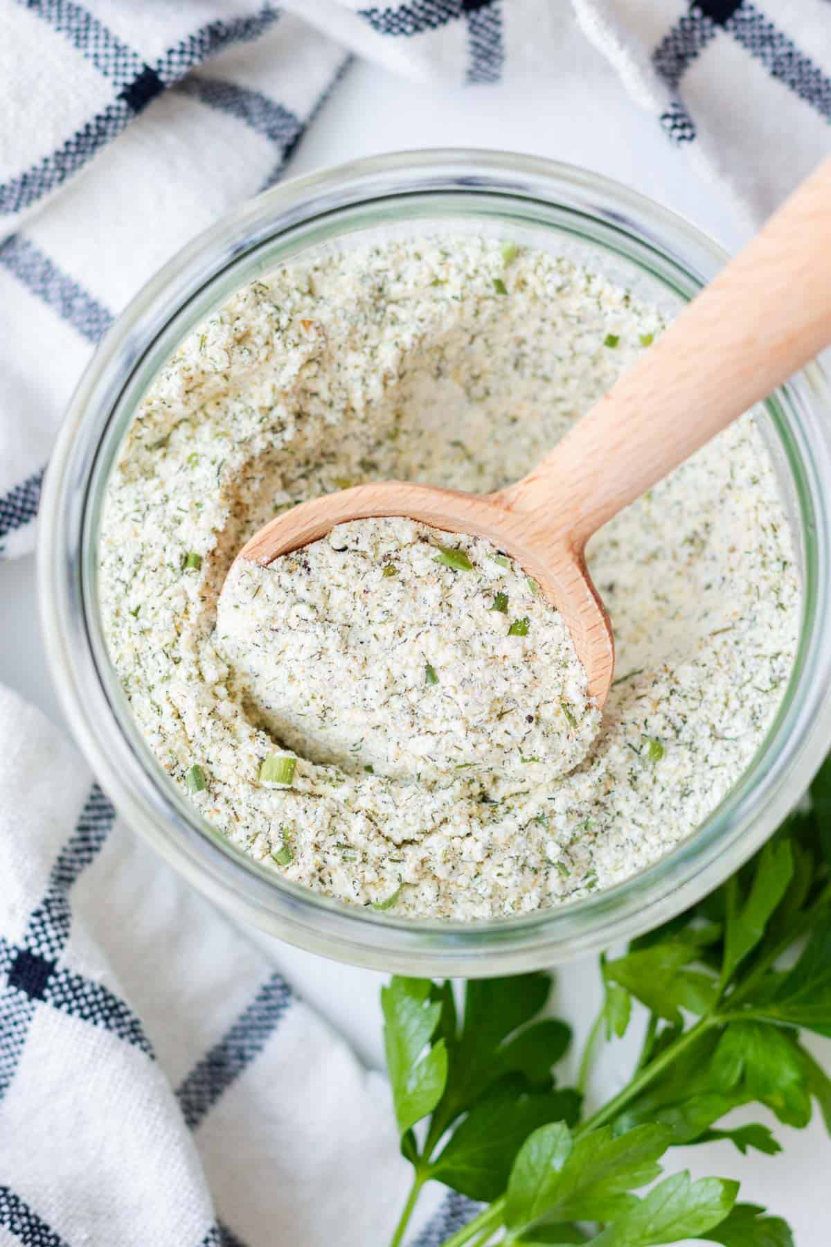 A round wooden serving spoon in a jar of ranch seasoning mix.