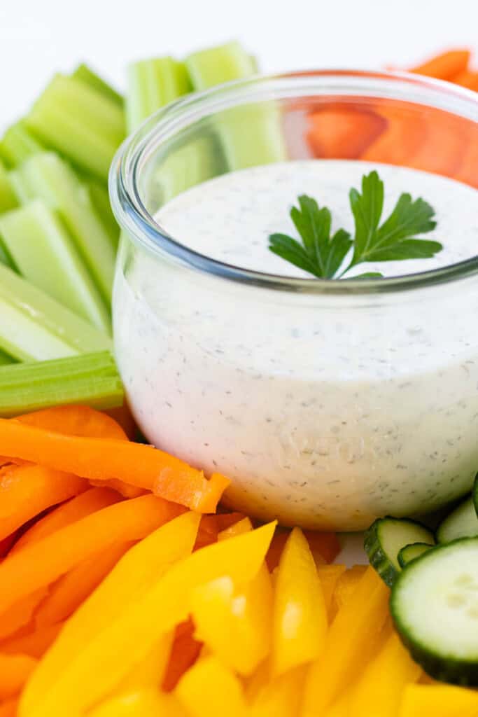 A jar full of ranch dressing nestled into a bed of fresh vegetables.