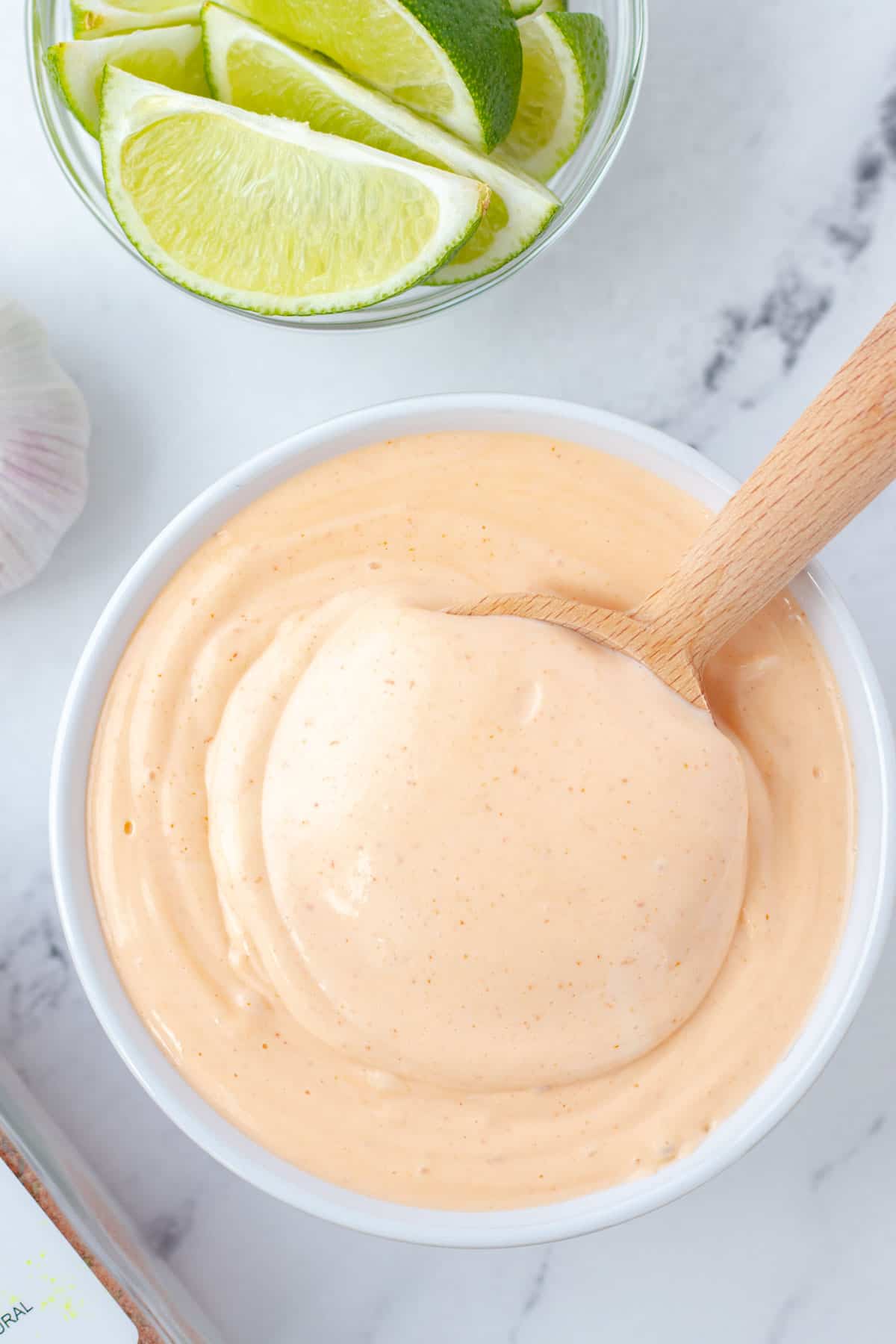 A bowl full of spicy mayonnaise with a wooden spoon and limes on the side.