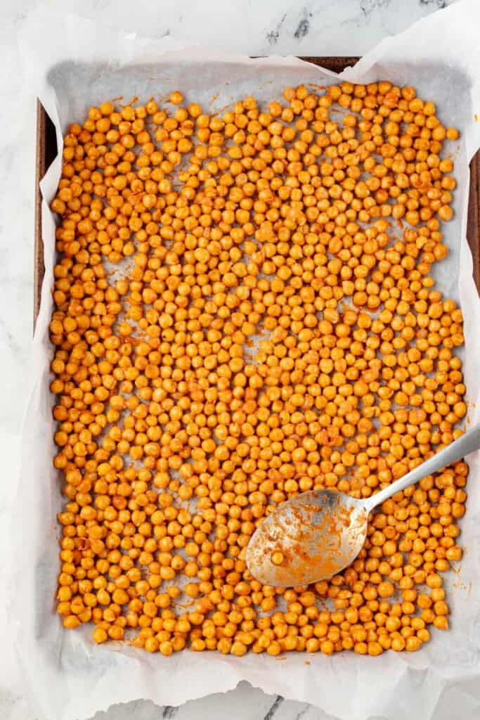 Spreading the seasoned chickpeas in a single layer on a baking sheet lined with parchment paper.