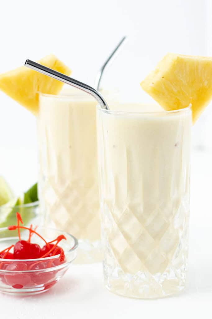Pouring blended piña colada into glasses and garnishing with a pineapple wedge.
