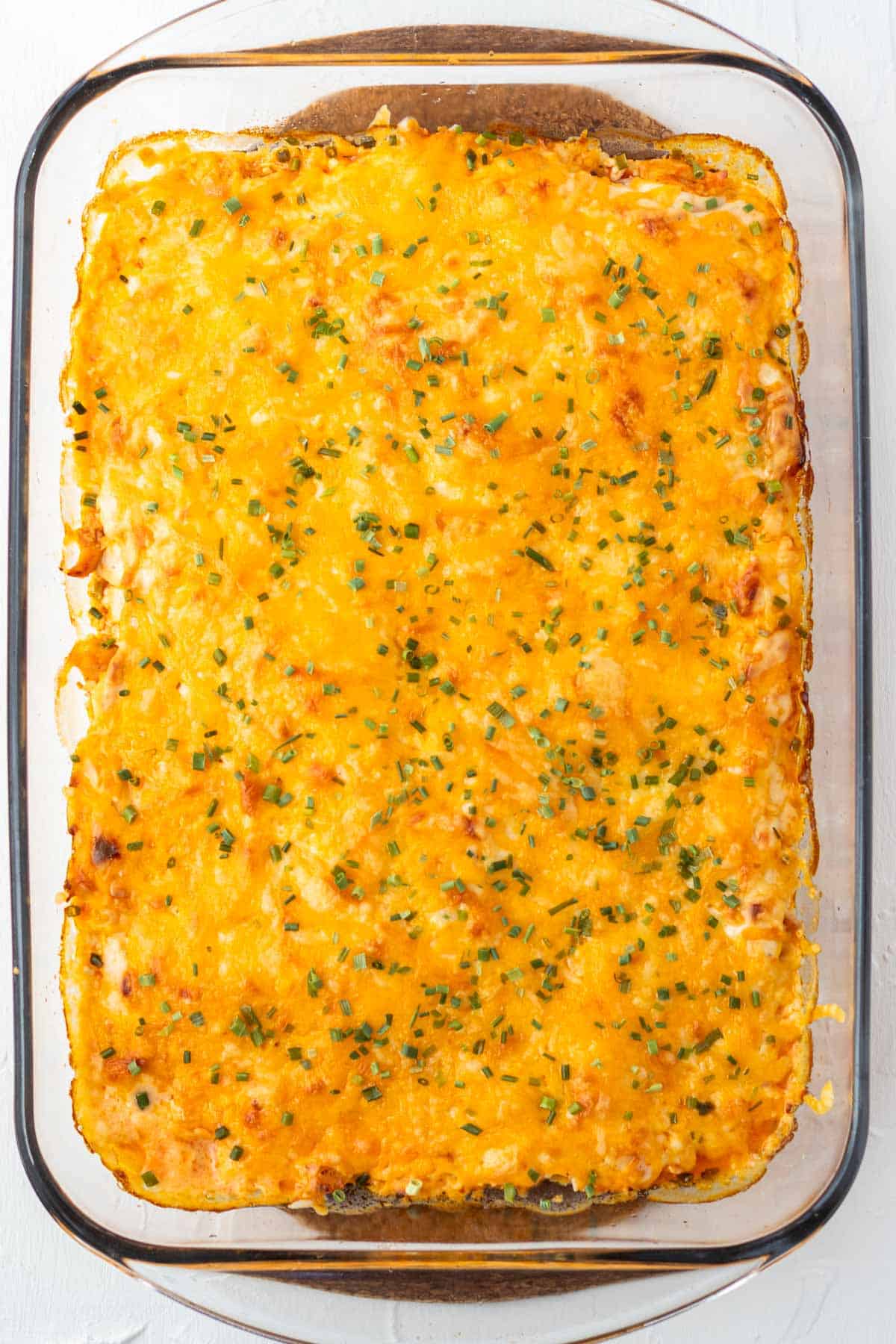 A casserole dish filled with baked buffalo chicken dip and topped with chives.