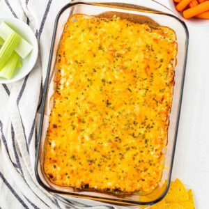 A pan of buffalo chicken dip after it has been baked with celery, carrots, and tortilla chips on the side.