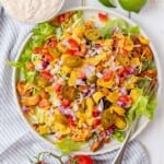 A white plate filled with chicken taco salad with dressing on the side.