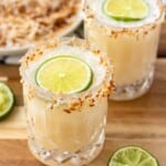 Two coconut margaritas rimmed with toasted coconut and topped with a wheel of lime.