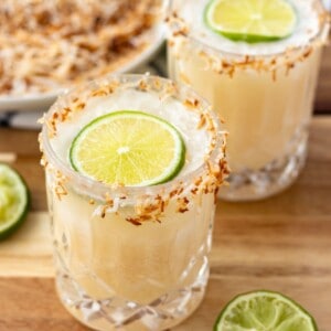 Two coconut margaritas rimmed with toasted coconut and topped with a wheel of lime.