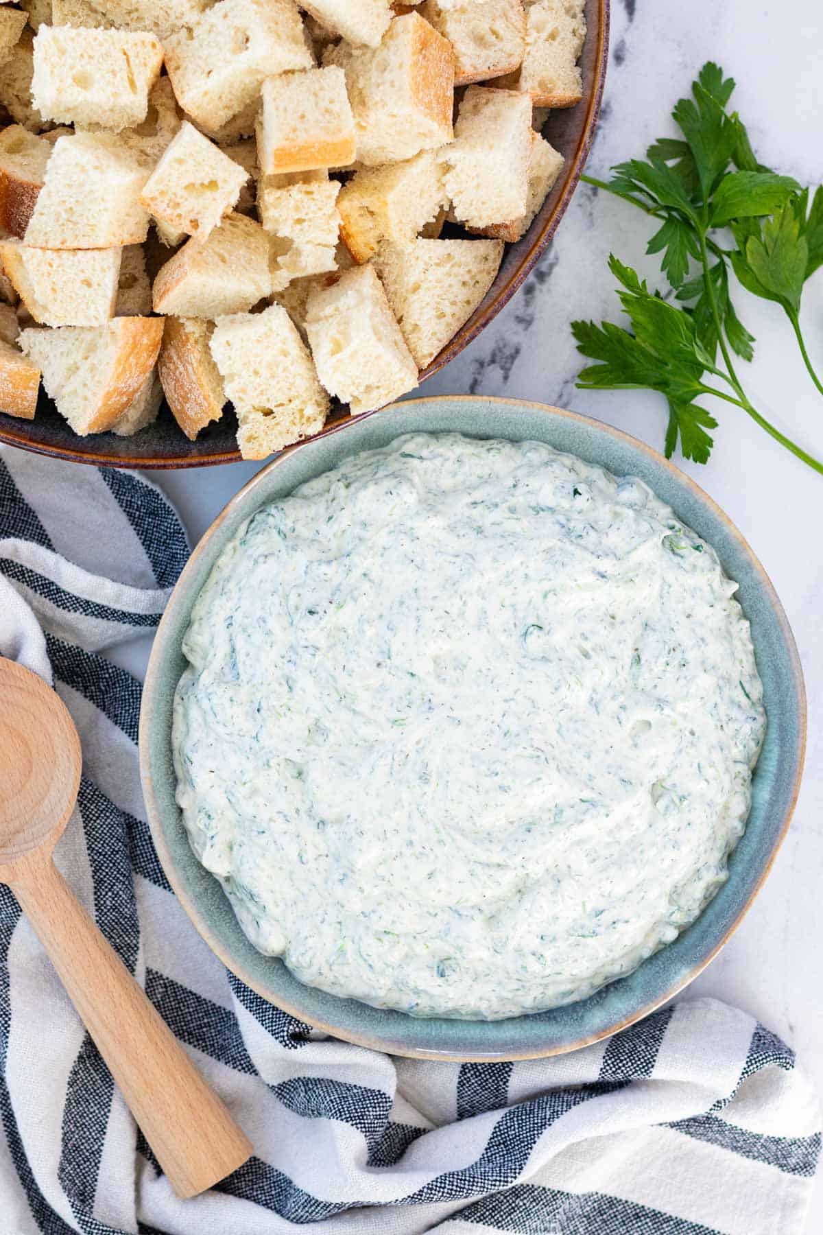 A blue serving bowl filled with spinach dip with a bowl of sourdough bread for dipping on the side.
