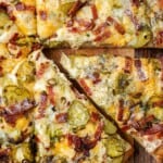 A whole dill pickle pizza sliced with one piece being pulled out.