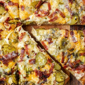 A whole dill pickle pizza sliced with one piece being pulled out.