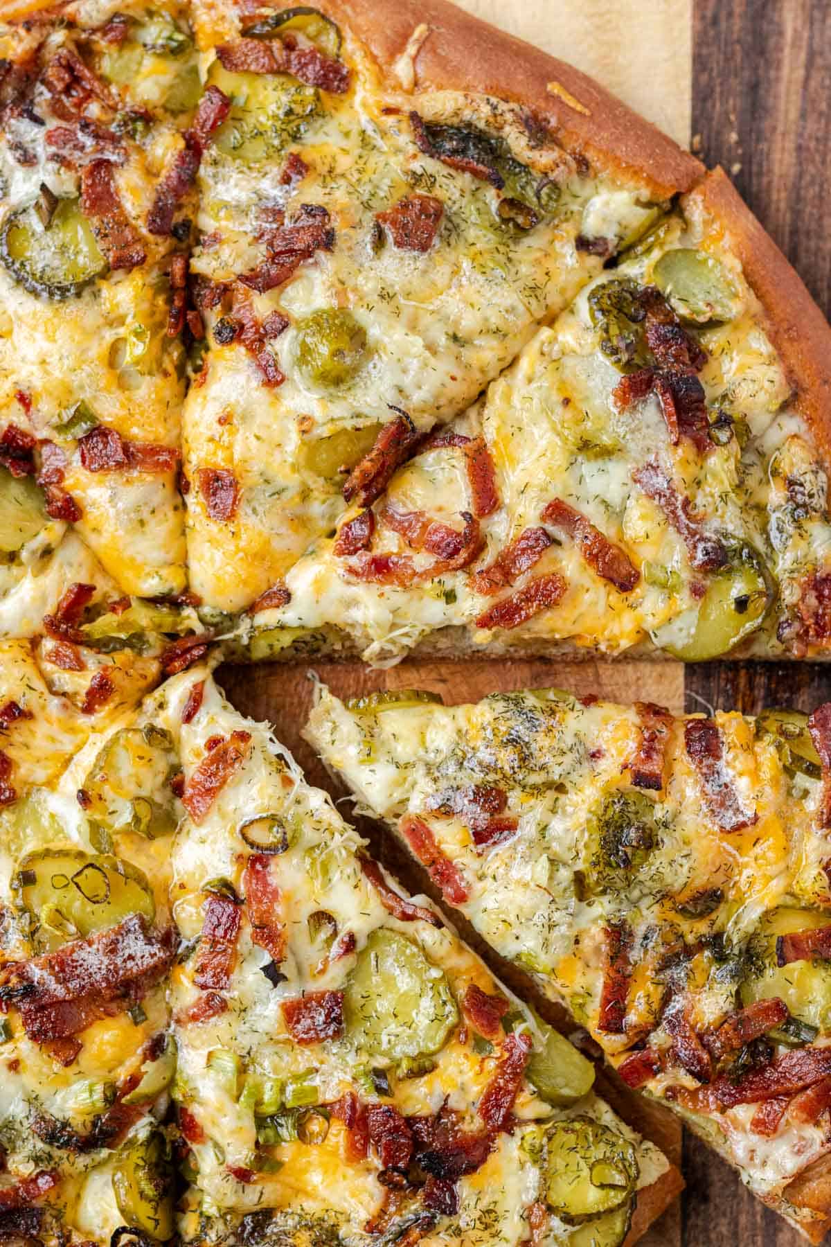 A whole dill pickle pizza sliced with one piece being pulled out.